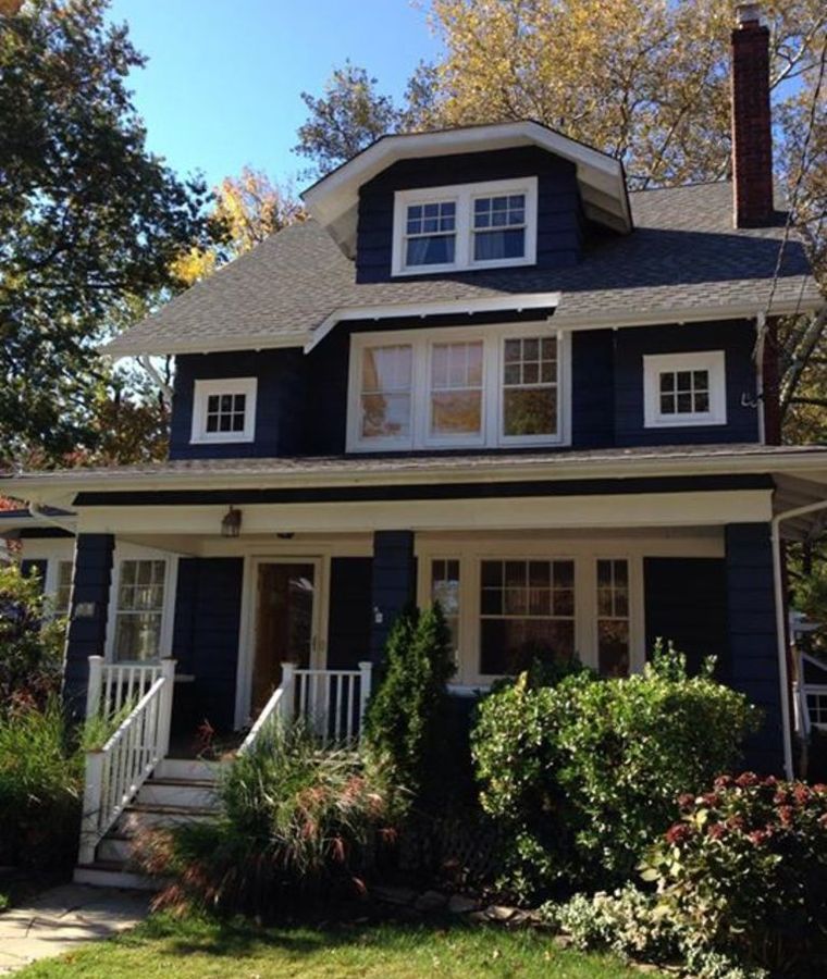 Navy craftsman house with a white porch and green shrubs