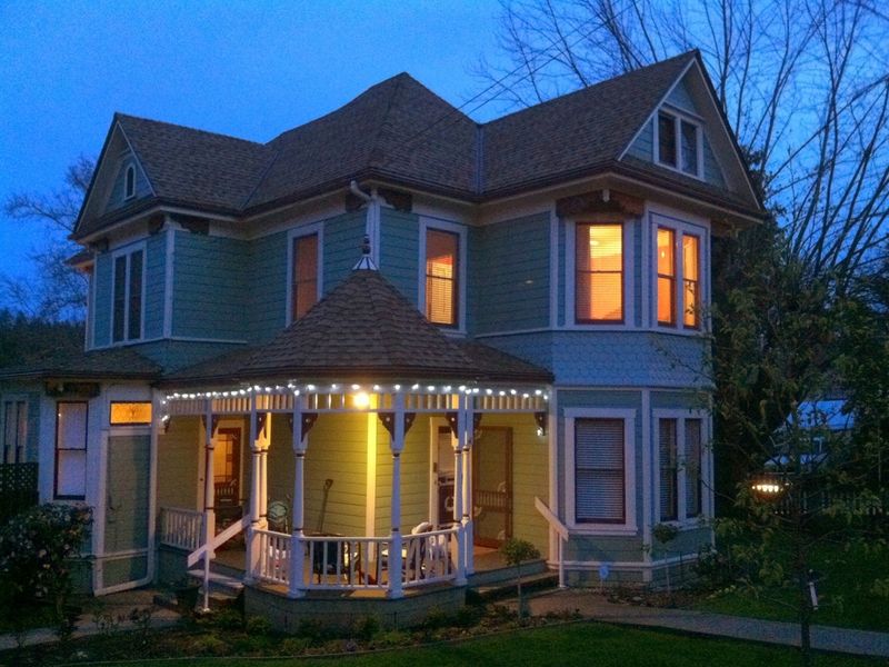 Victorian home with its porch lit up at dusk